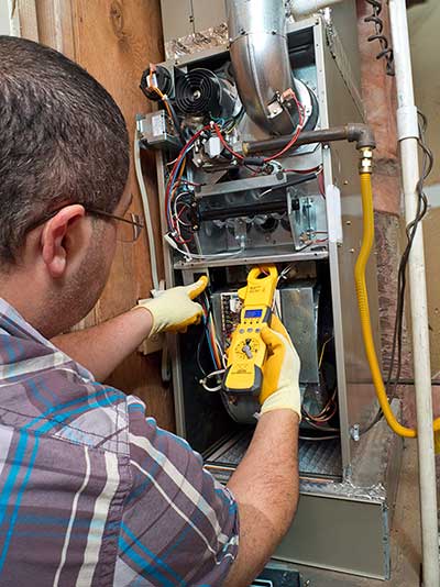 Man with yellow gloves using a meter to inspect a furnace.