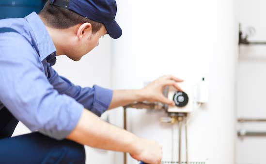 Man in blue shirt and cap adjusts a water heater thermostat.