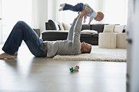 Man lying on back, lifting a child up in the air indoors on a rug; toy on floor.