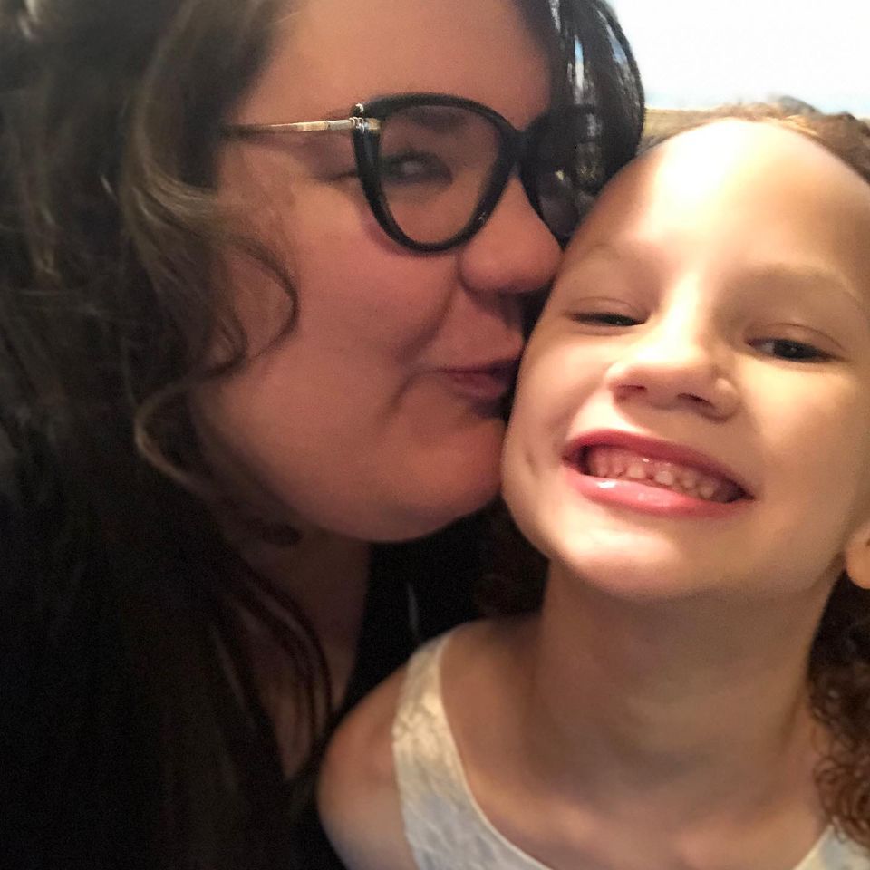A woman wearing glasses kisses a little girl on the cheek