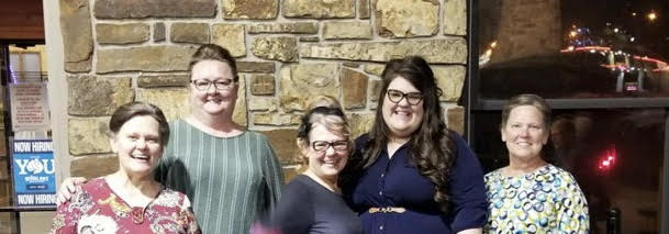 A group of women are posing for a picture in front of a brick wall.