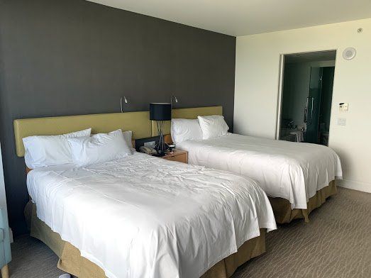 A hotel room with two beds and a gray wall.
