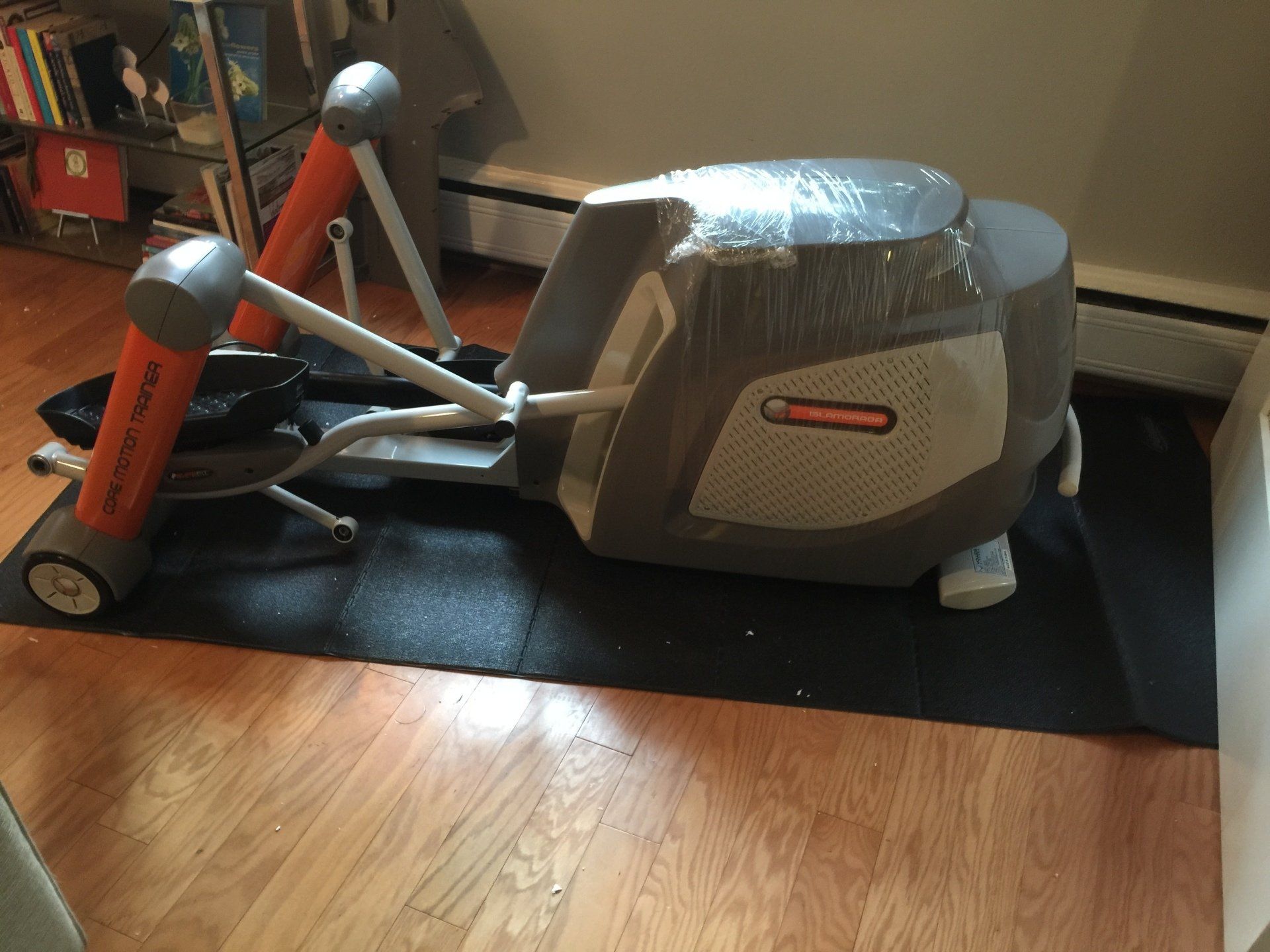 An elliptical is sitting on a black mat on the floor
