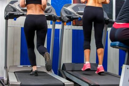 Two women are running on treadmills in a gym.