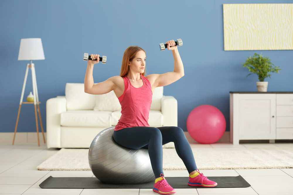 A woman is sitting on an exercise ball while holding dumbbells.