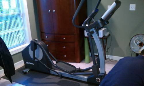 An elliptical machine is sitting in a room next to a window.