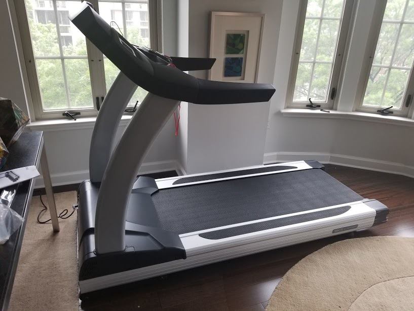A treadmill is sitting in a living room next to a window.