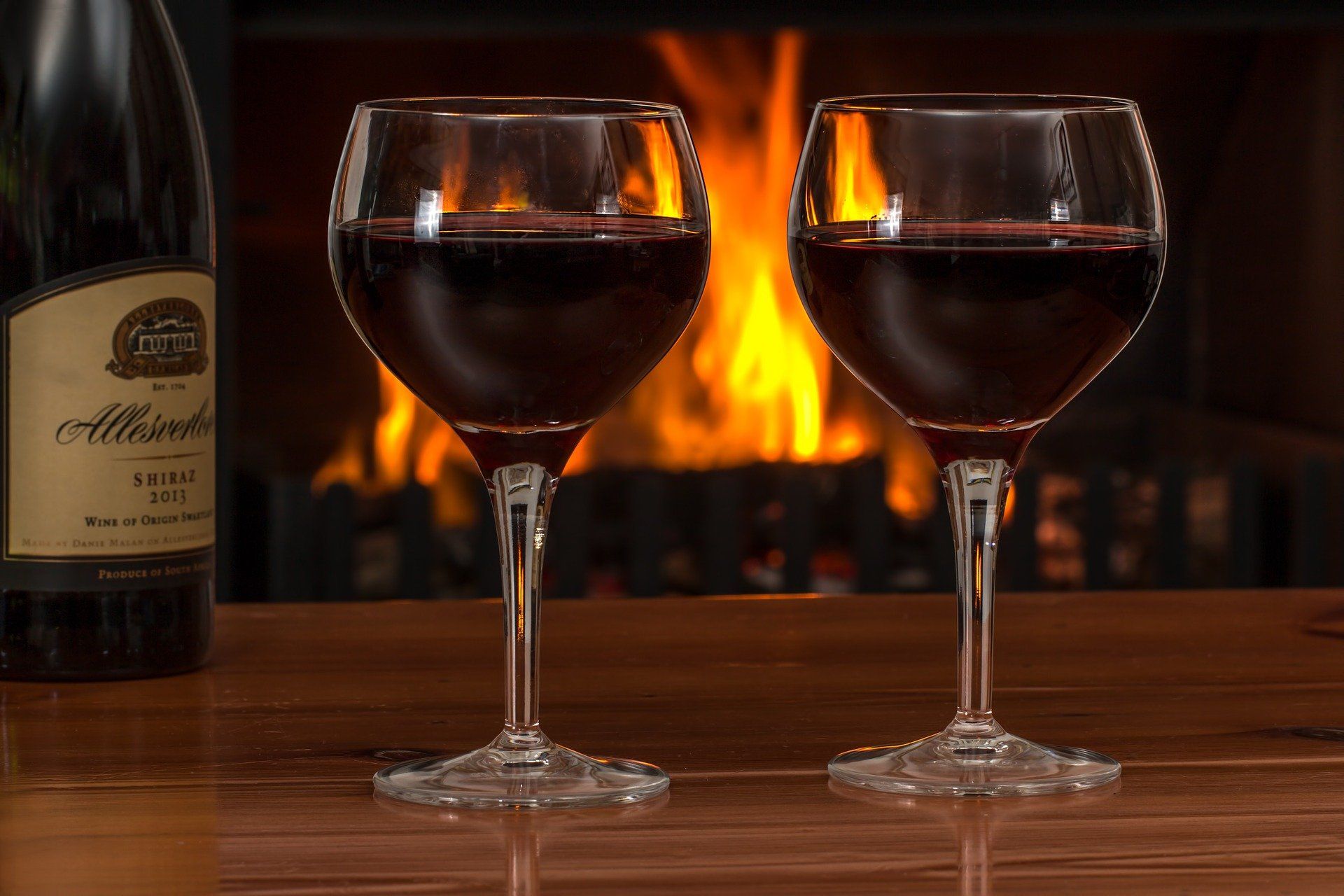Zwei Gläser Rotwein stehen auf einem Tisch mit Feuer im Hintergrund