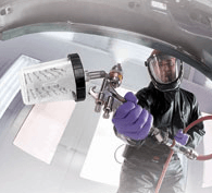 Technician in a protective suit spray-painting the inside of a vehicle with a spray gun