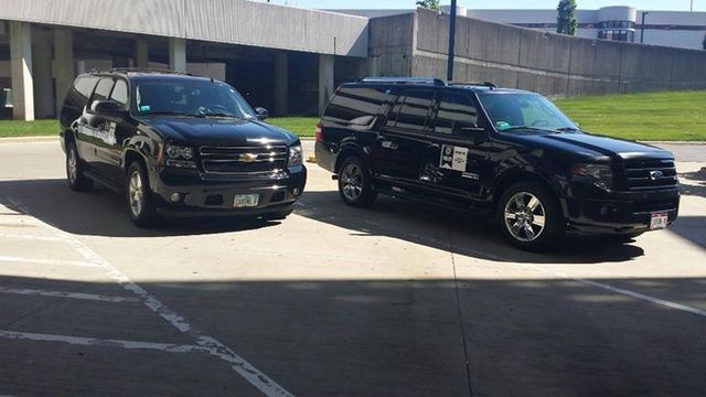 Two black SUVs parked outside a building. One has a longer body.