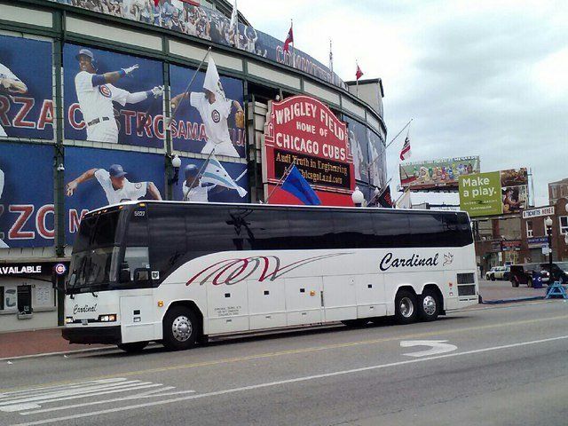 White Cardinal bus parked outside Wrigley Field. Mural of baseball players visible.
