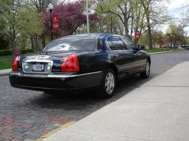 Black Lincoln Town Car parked on cobblestone street near a sidewalk and trees.