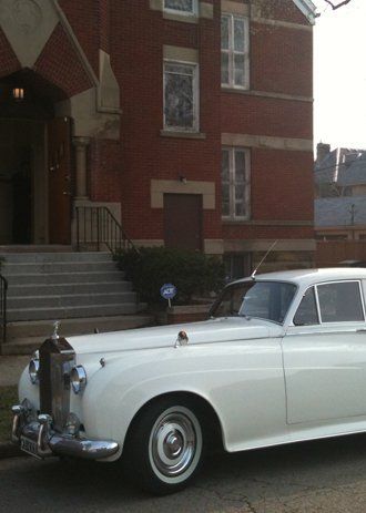 White Rolls-Royce parked in front of a red brick building with steps.