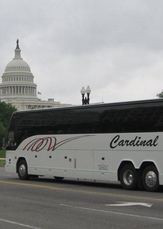 White Cardinal bus in front of the U.S. Capitol building on a cloudy day.