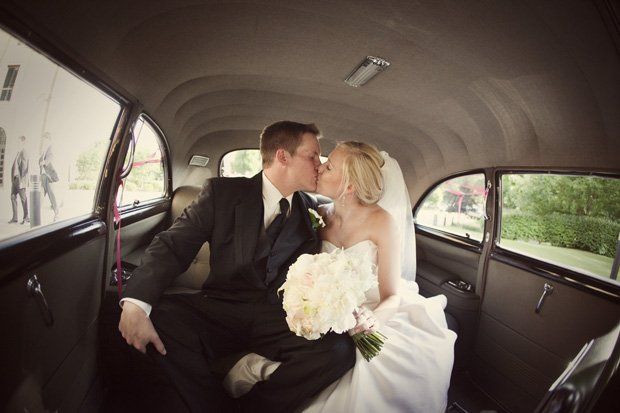 Couple kissing inside a vintage car after wedding. The bride holds flowers.