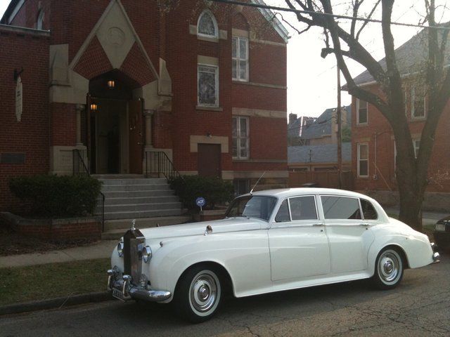 White classic Rolls Royce parked in front of a red brick church.