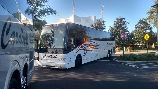 White Cardinal bus parked outside a building with unique architecture, sunny day.