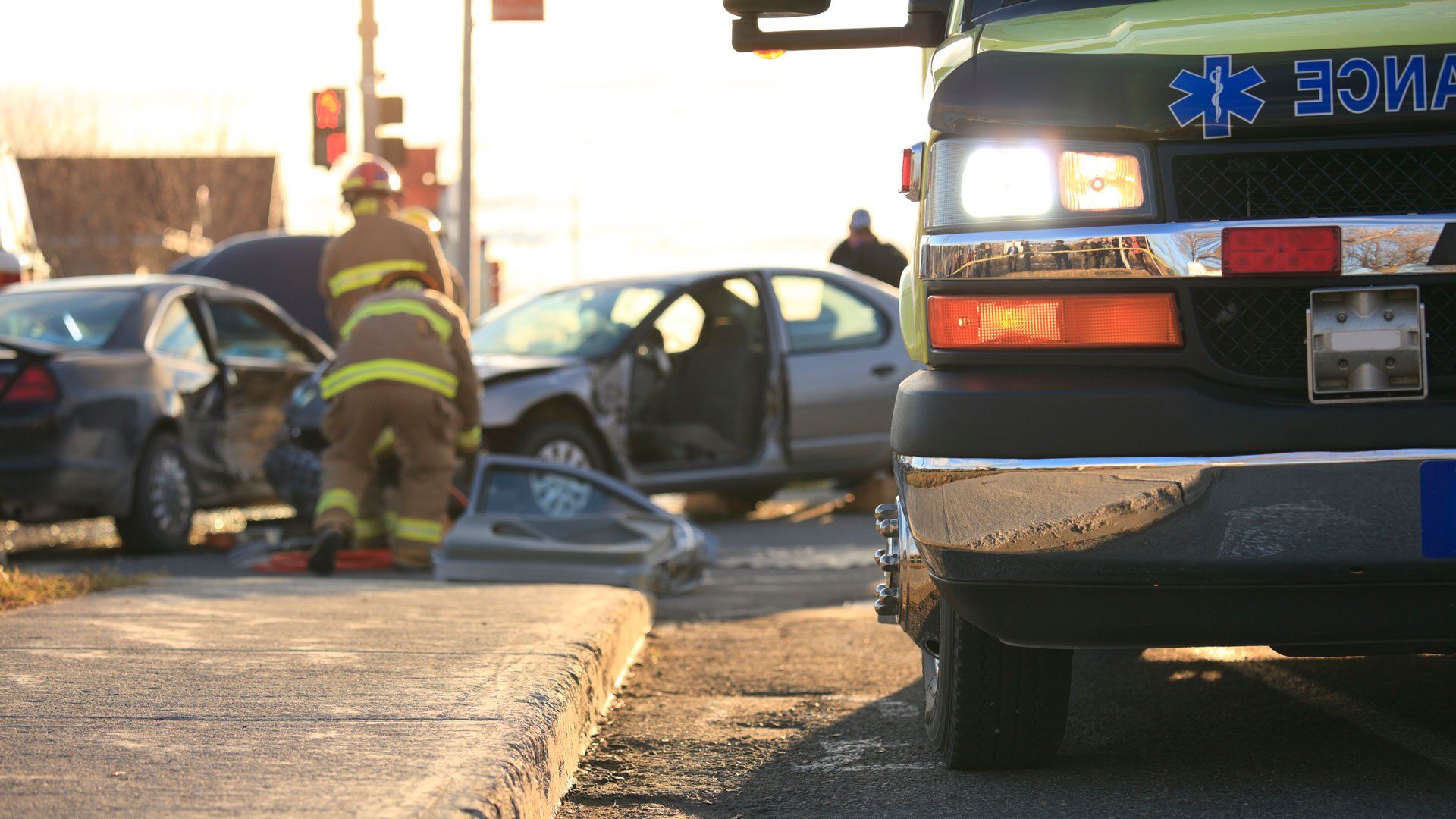 Emergency responders at a car accident scene with ambulance, damaged vehicles, and firefighters.