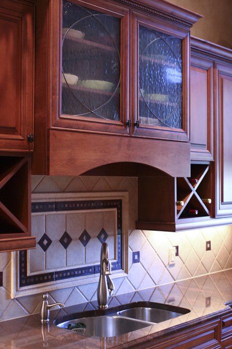 Decorative valance under glass doors flanked by diamond wine racks and tile backsplash.