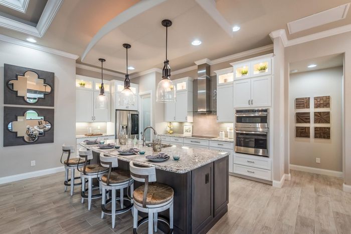 Illuminated stacked upper cabinets around kitchen with stone tops and stainless appliances. Large elegant pendant lights