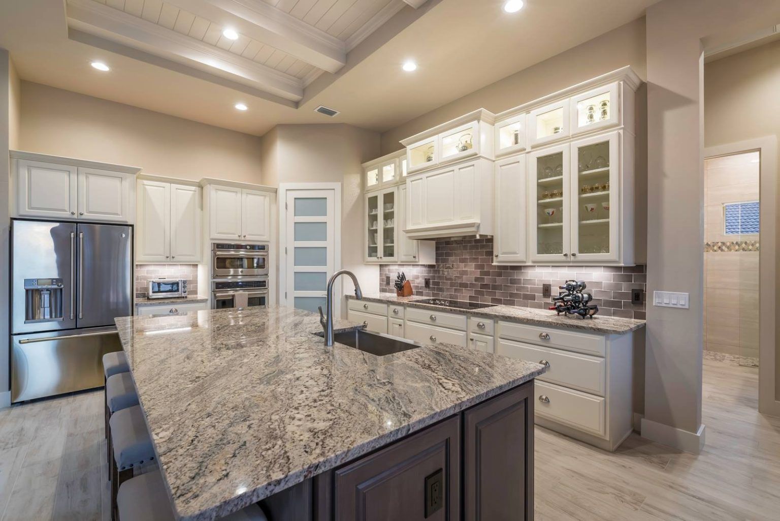 White shaker cabinetry with tile backsplash. Tray ceiling with shiplap and beams.