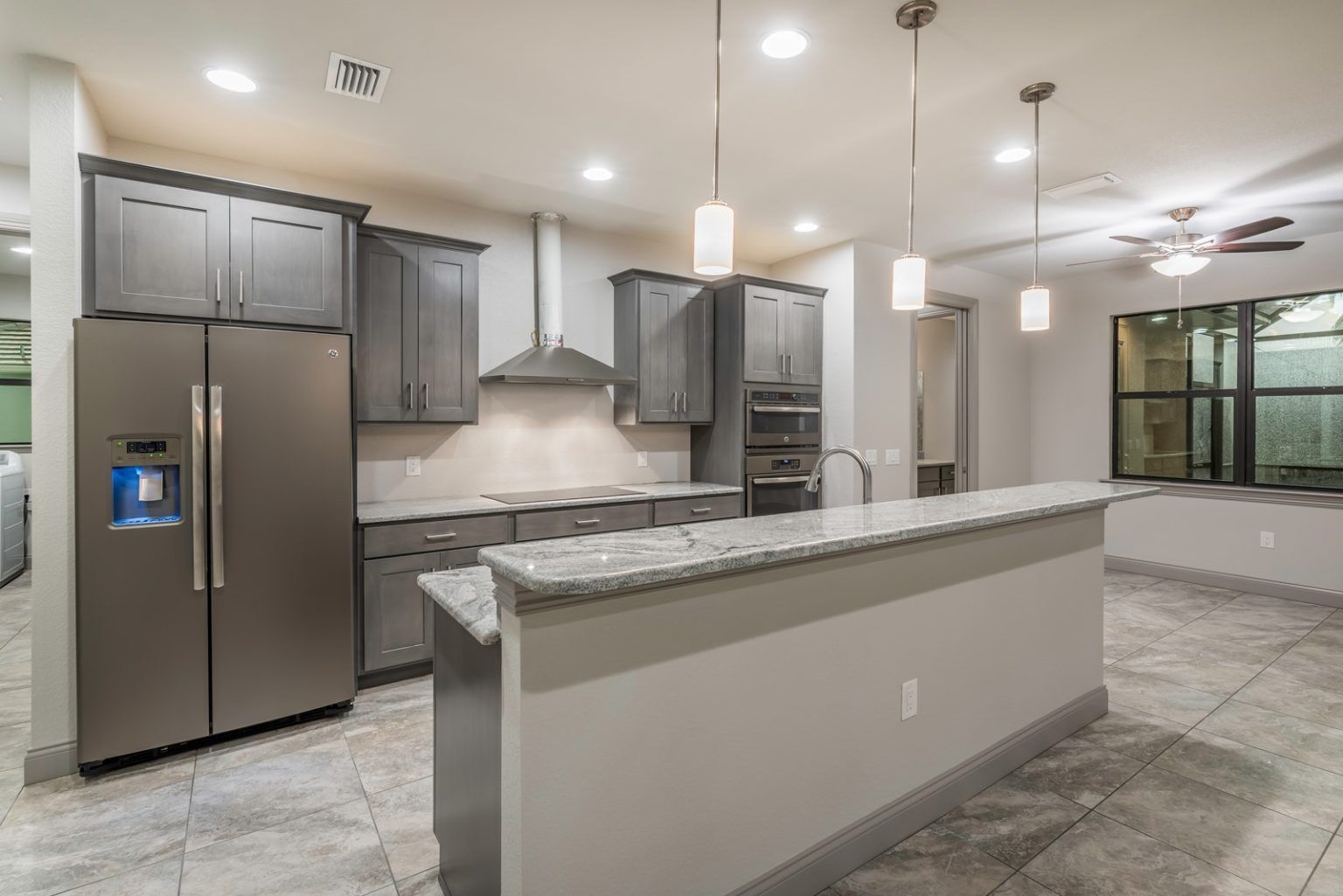 Grey stained cabinetry in kitchen with raised bar top at the island. Wall oven cabinet with stainless appliances.