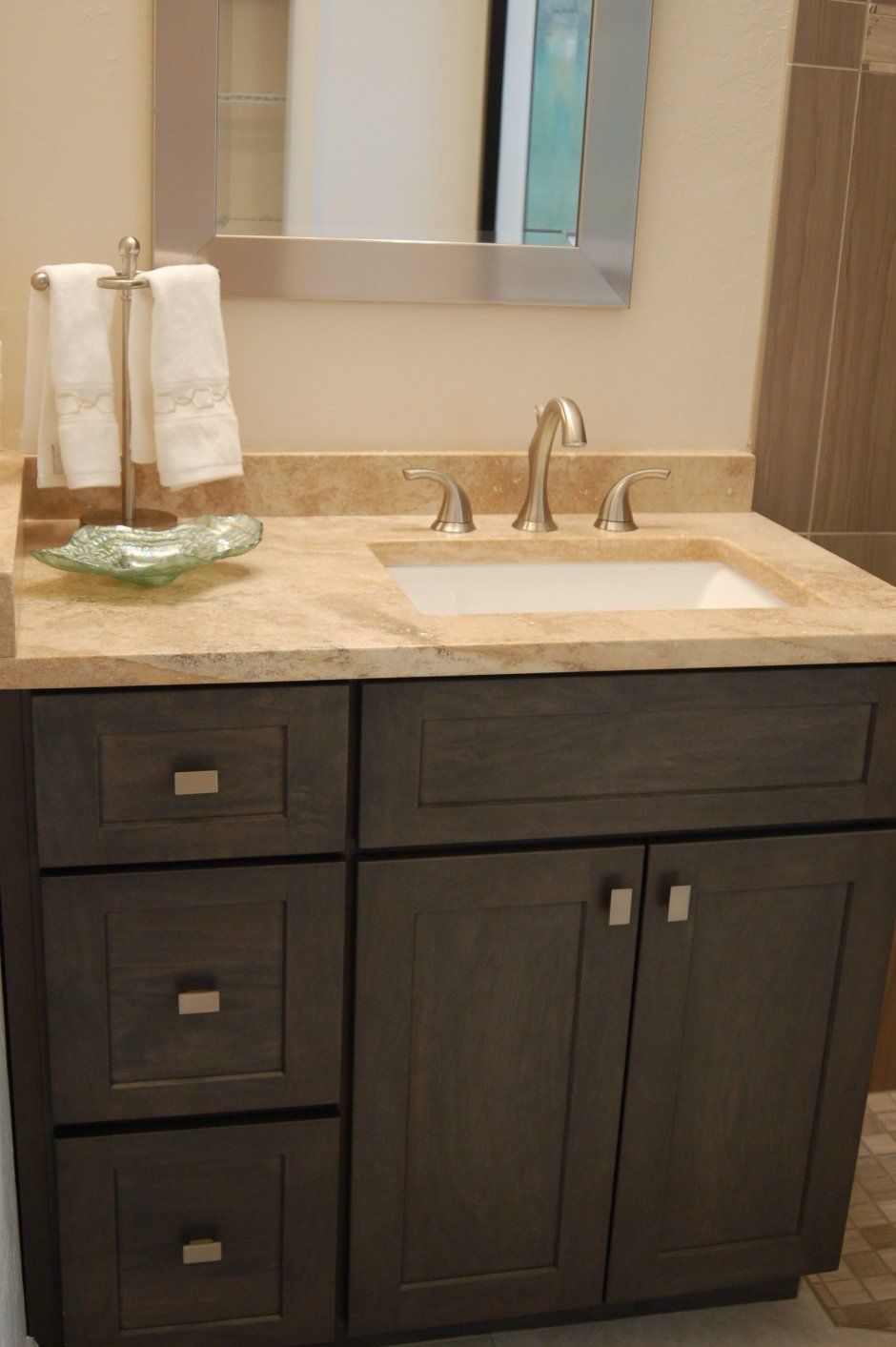 Tan stone countertop on top of dark stained shaker style cabinets in bathroom remodel project.