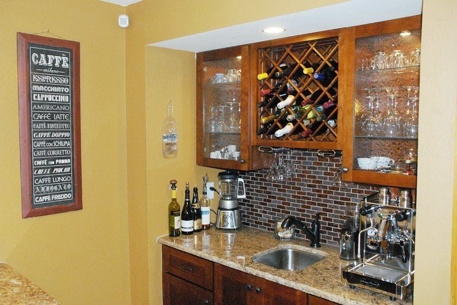 Rich stained oak cabinetry in a wet bar remodel with granite counter. Wine rack, stemware holders, bar sink, and glass doors.