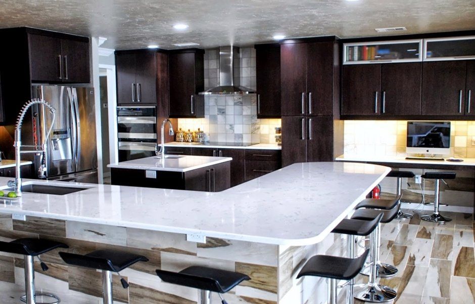 Large L-shaped island wrapped with matching tile. White quartz countertops and dark cabinetry.