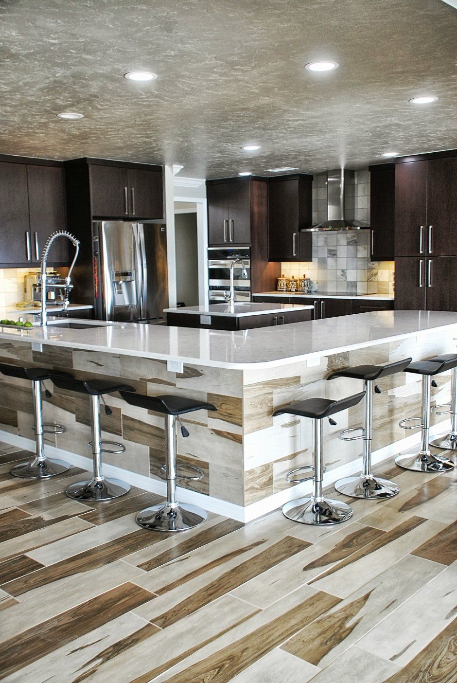 Recessed lighting in unique textured ceiling above cozy dark stained kitchen with tile backsplash.