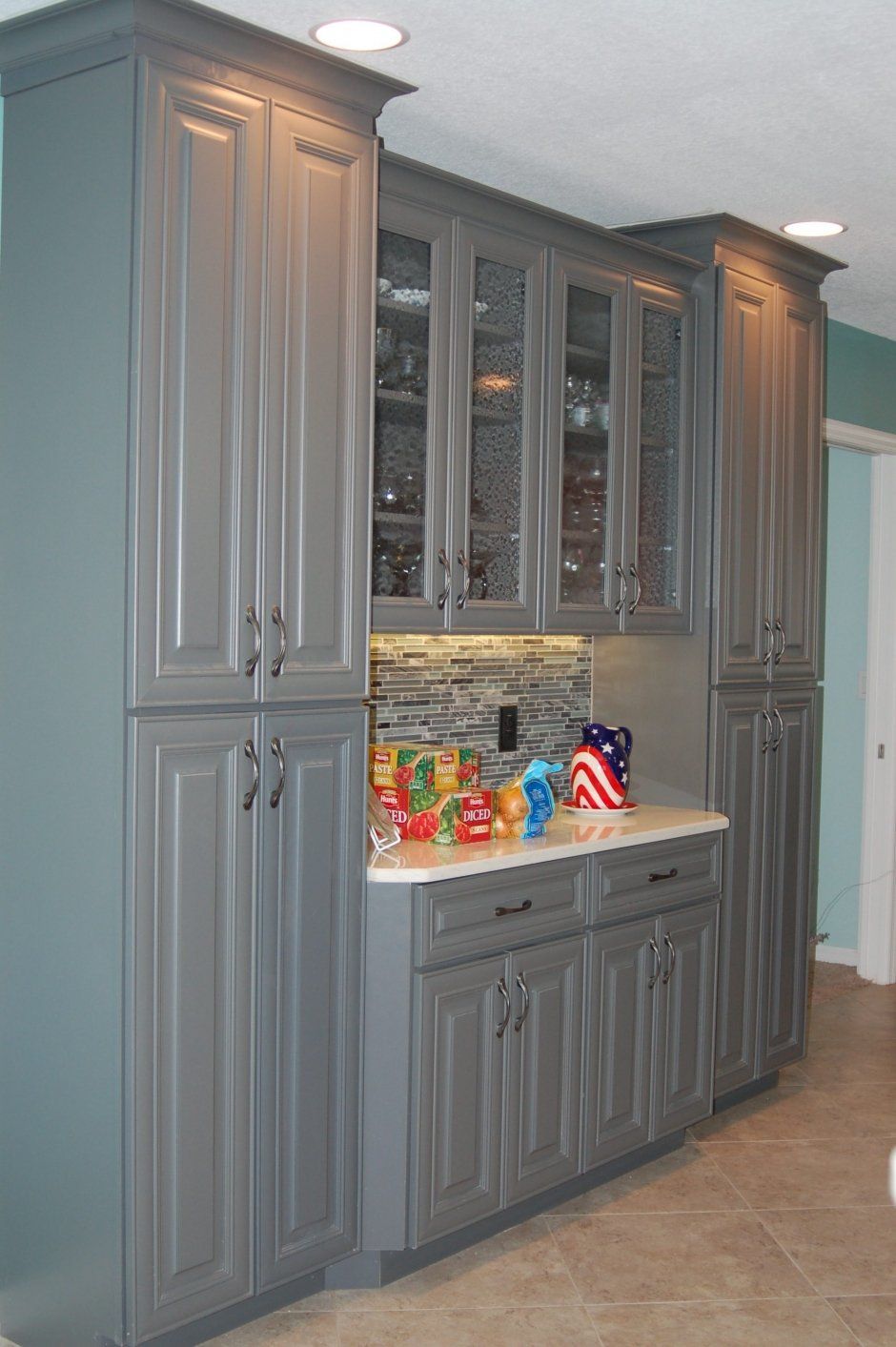 Raised panel doors on grey face frame cabinetry. Glass door inserts.