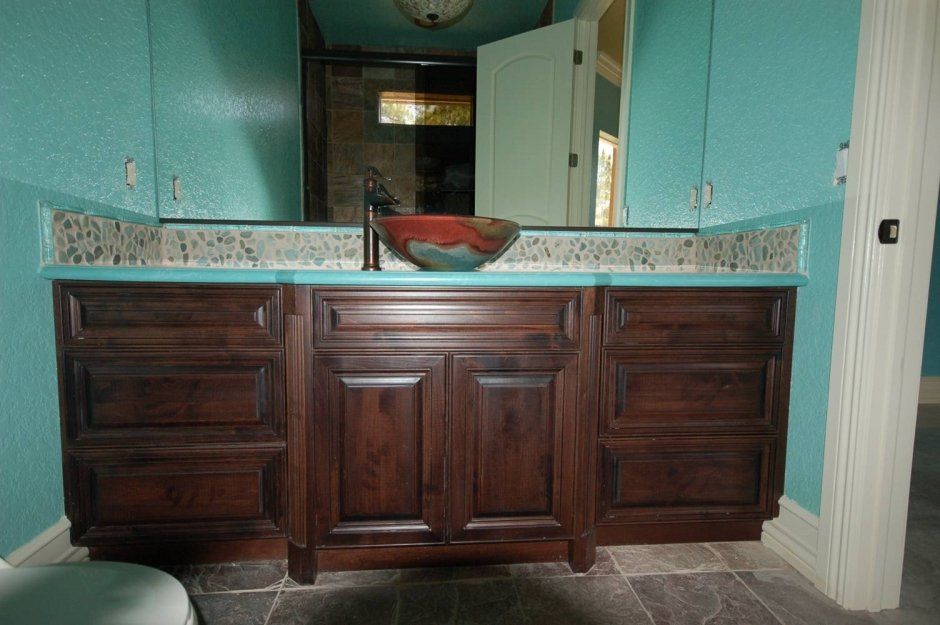 Teal wall paint behind dark stained cabinetry with multi-colored vessel sink in bathroom remodel.