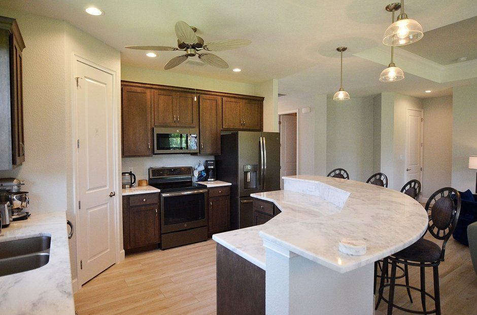Curved raised bar top overlooking dark stained wood cabinetry in the kitchen. White marbled quartz countertops.