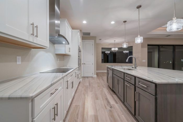Decorative metal hood over sleek cooktop. Pendant lights over the accent island with quartz tops all around.