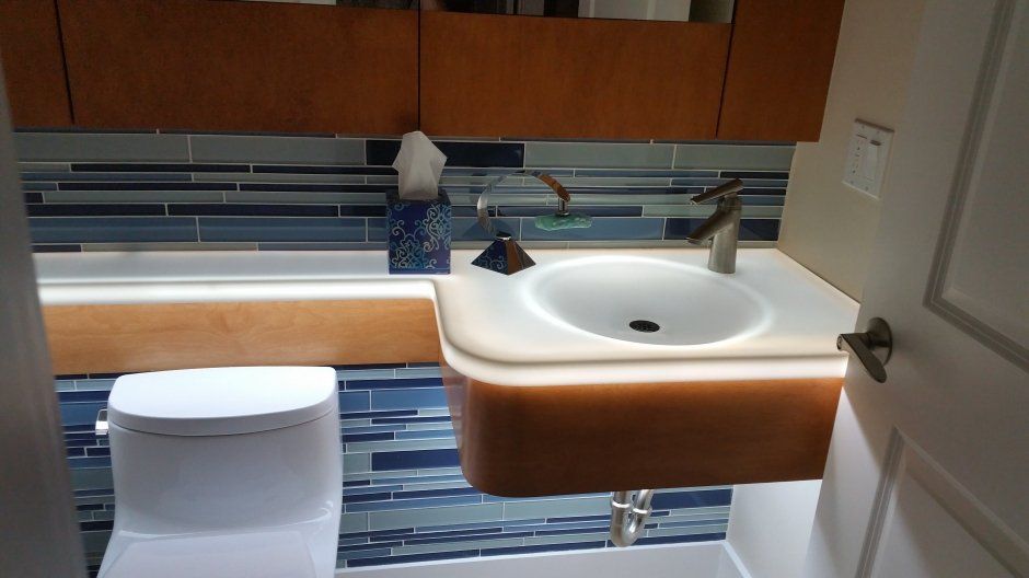 Underlit stone top glowing with abstract blue tile backsplash and modern toilet.