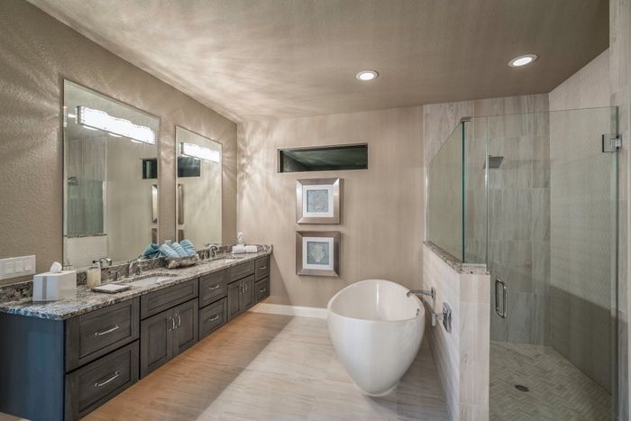 Floating vanity remodel with stone countertops, freestanding bathtub and tile shower. Light fixtures on large mirrors.