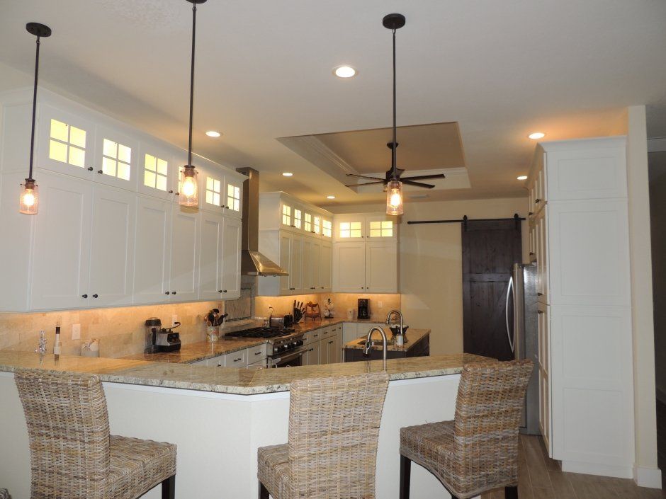 Wicker chairs at raised bar overlooking white shaker kitchen remodel. Dark stained barn door accent.