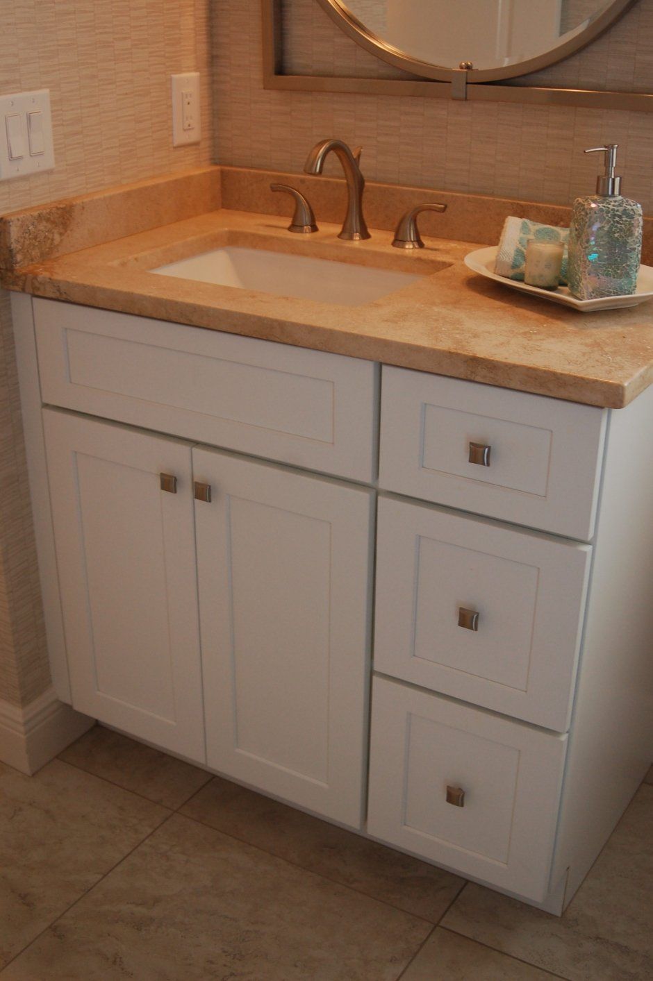 Tan countertop material with porcelain sink above white shaker cabinetry. Bathroom remodel.