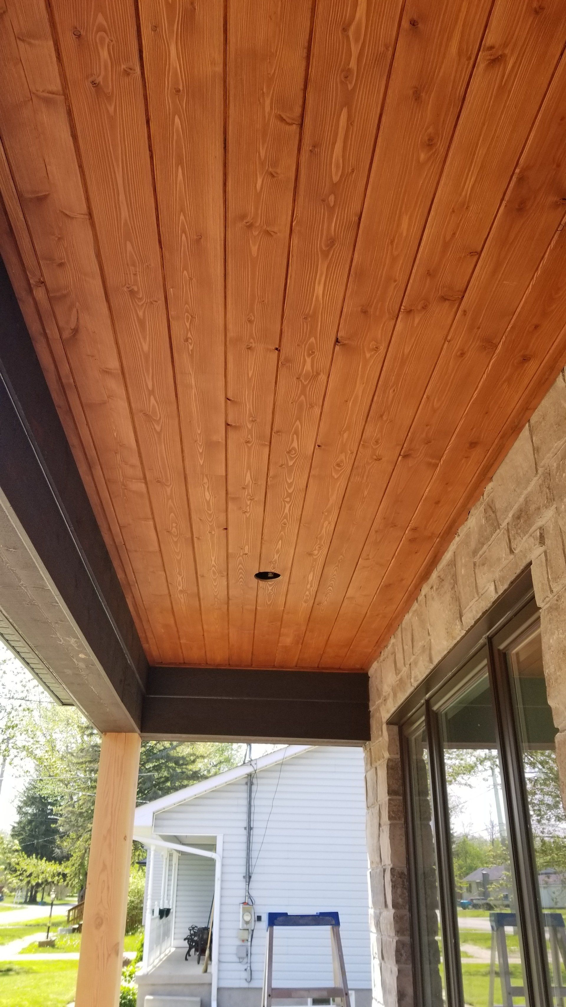 The ceiling of a porch with wood paneling and a ladder.
