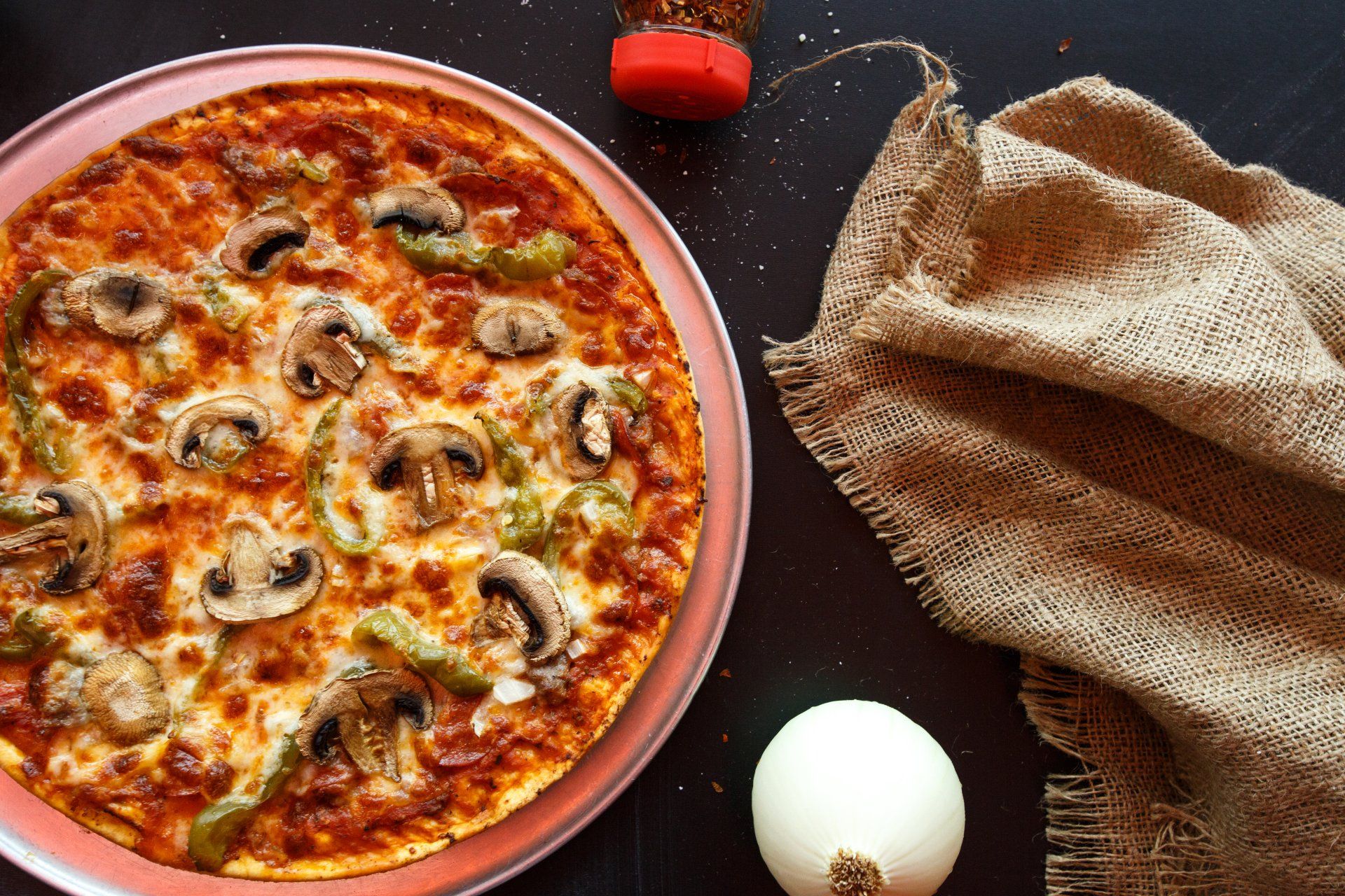 A pizza with mushrooms , peppers and cheese on a plate on a table.