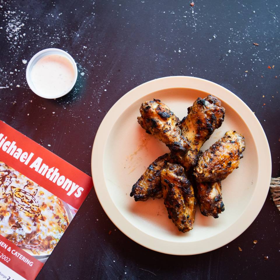 A plate of chicken wings next to a michael anthonys cookbook