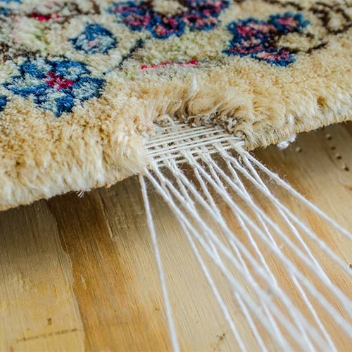 Close-up of a rug's edge, showing white threads unraveling from the beige and floral patterned surface.