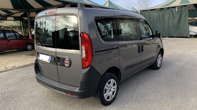 Furgone compatto grigio parcheggiato all'aperto su un piazzale ghiaioso vicino a tende e un'altra auto