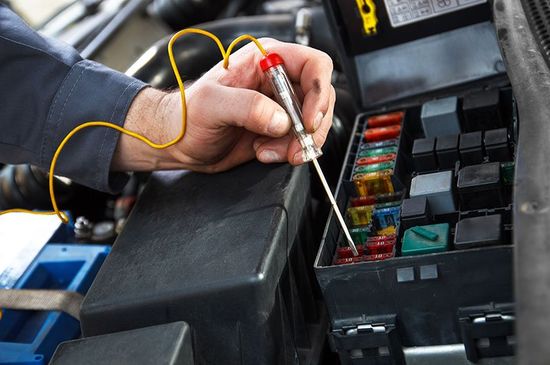 la mano di un meccanico con un cacciavite tester in mano mentre controlla una batteria di una macchina