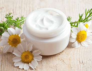 un barattolo di crema aperta con di fiori di camomilla accanto