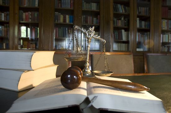 una bilancia a due piatti che pende dal lato destro, un libro aperto e sopra un martello di legno e sulla sinistra altri due grandi libri una bilancia a due piatti che pende dal lato destro, un libro aperto e sopra un martello di legno e sulla sinistra altri due grandi libri