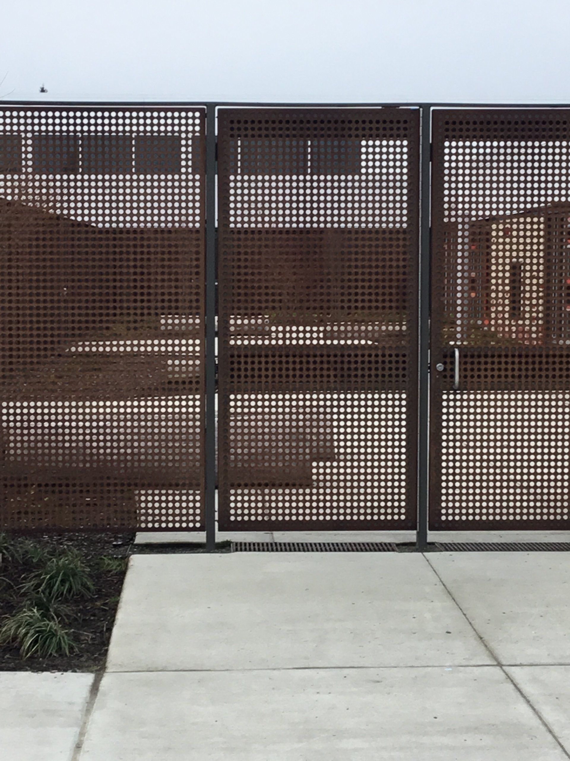 Brown metal gate beside a concrete sidewalk and a white fence in a residential area