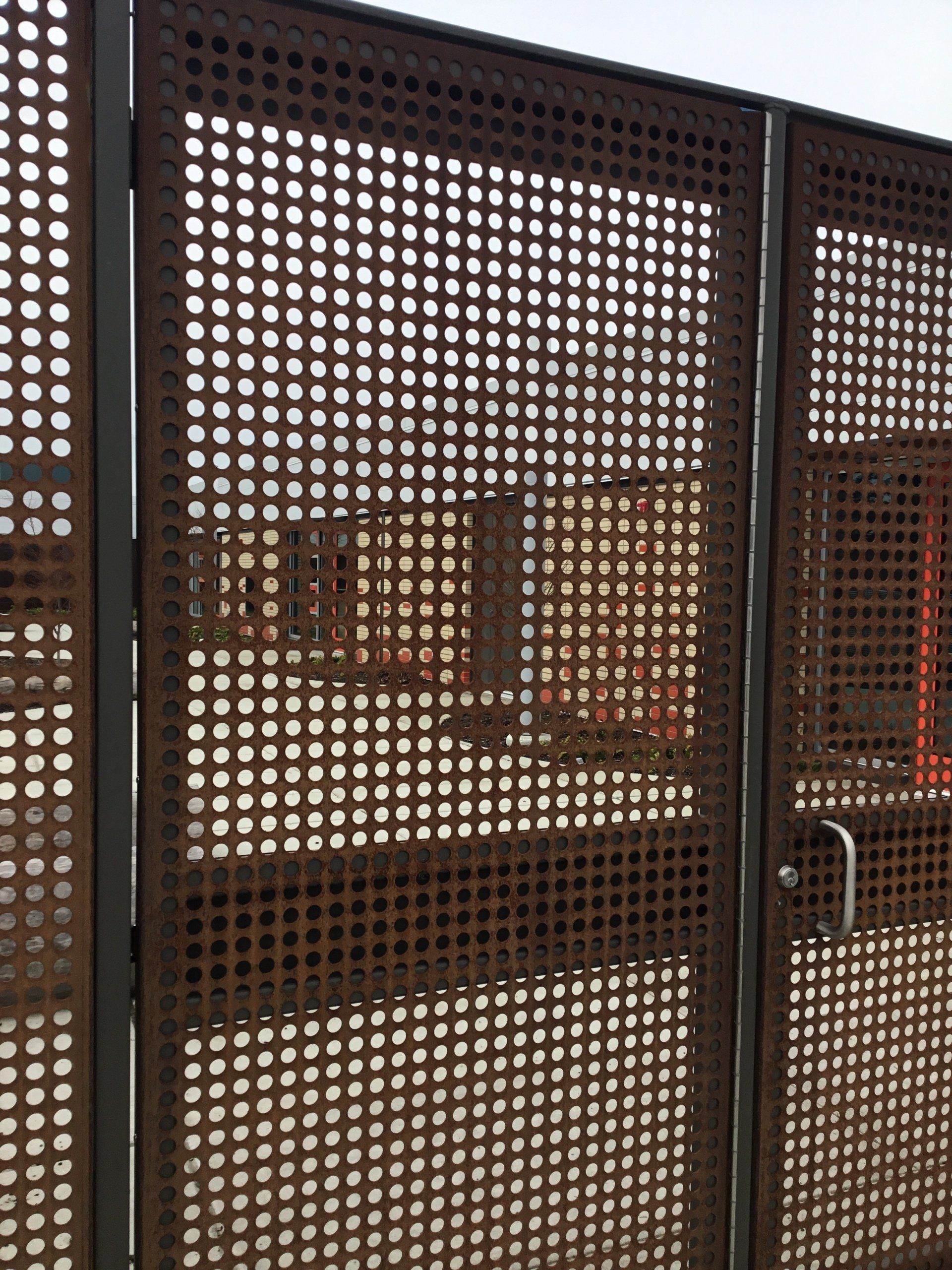 Brown perforated metal gate with a small latch, opening to a courtyard beyond.