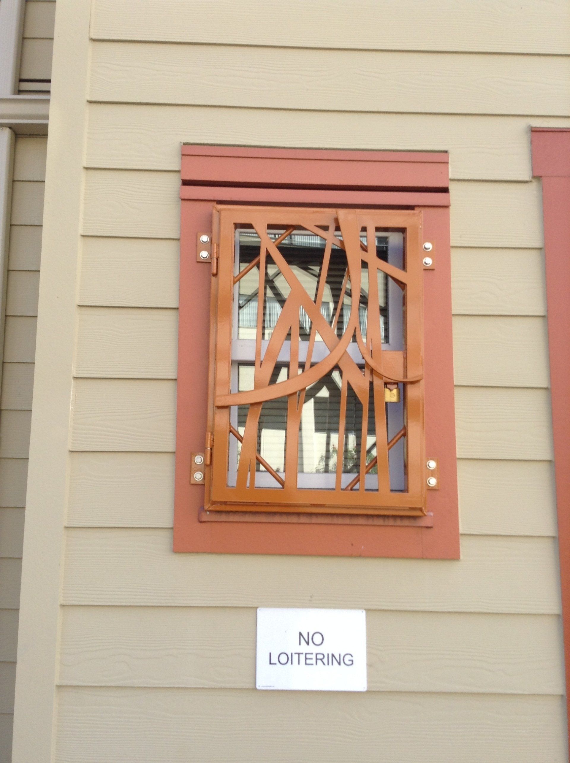 Orange barred window on beige siding with a “No Loitering” sign below.