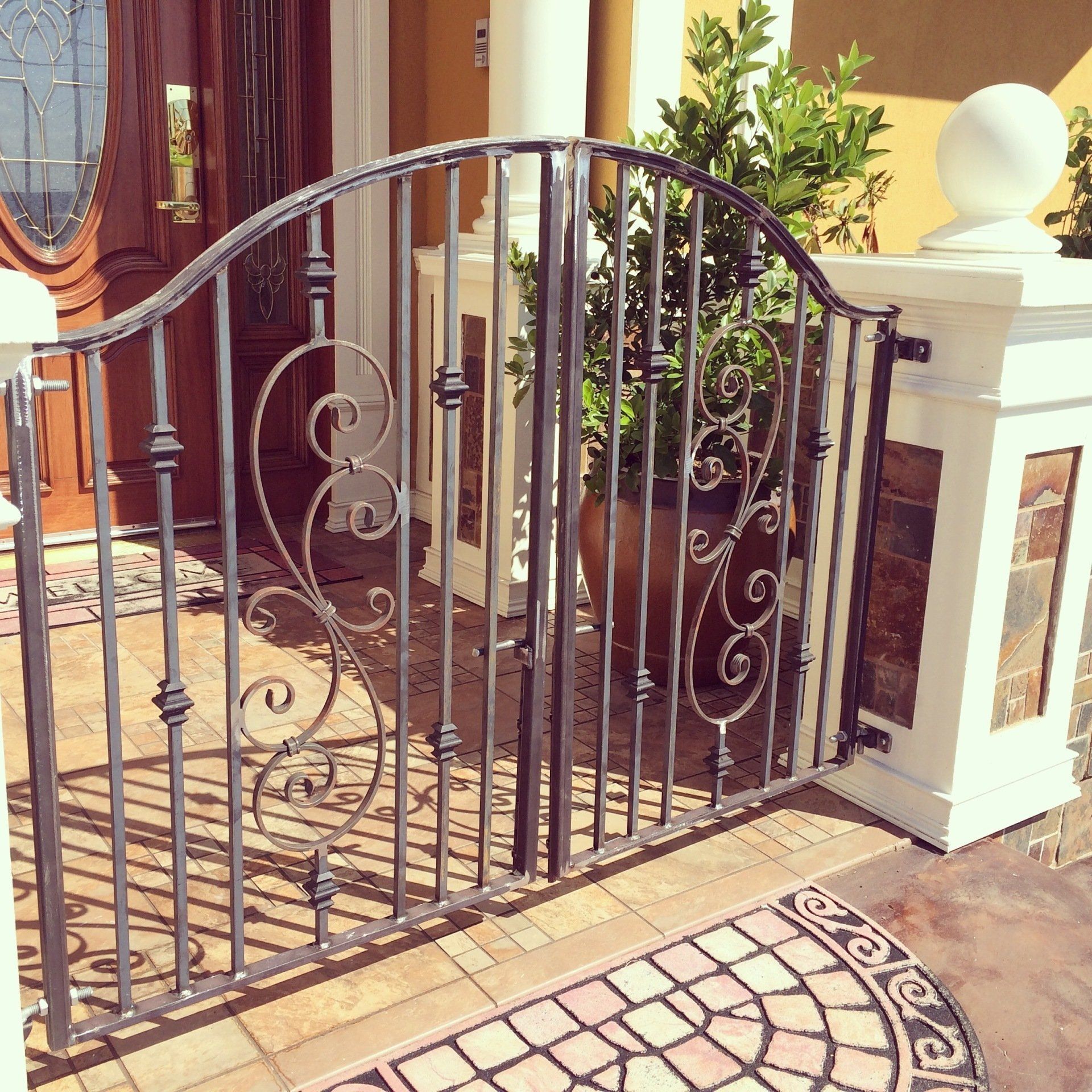 Black wrought-iron gate at a stone entrance with white pillars and potted plants